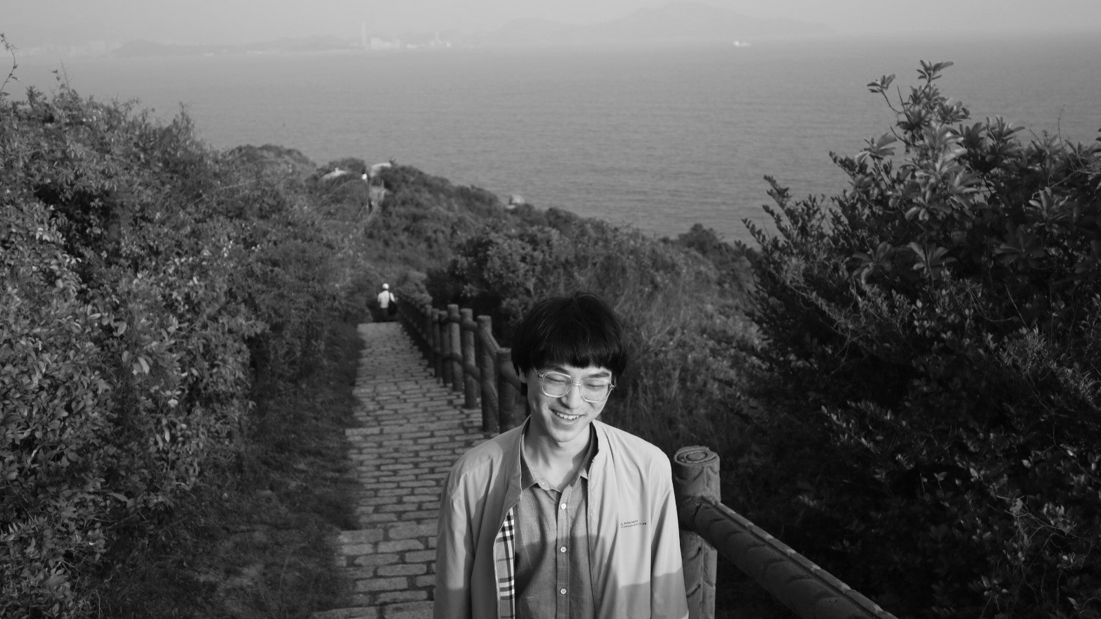 Yigang is standing on the island hillside stairs, smiling facing the sunset.